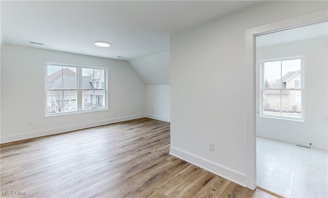 additional living space with light wood-type flooring, visible vents, baseboards, and lofted ceiling