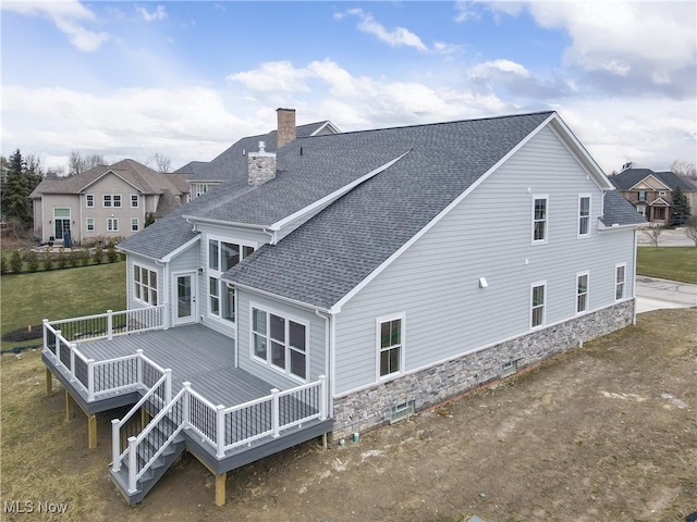 rear view of house featuring a deck, roof with shingles, a yard, and a chimney