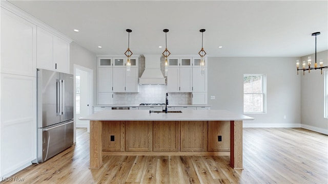 kitchen featuring custom range hood, appliances with stainless steel finishes, a sink, light countertops, and backsplash