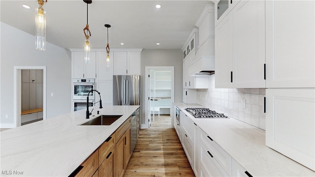 kitchen featuring tasteful backsplash, custom range hood, appliances with stainless steel finishes, light wood-style floors, and a sink