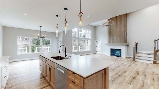 kitchen with a sink, stainless steel dishwasher, light wood finished floors, plenty of natural light, and an inviting chandelier