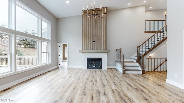 unfurnished living room with a chandelier, a high ceiling, wood finished floors, visible vents, and baseboards