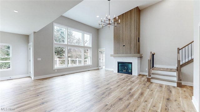 unfurnished living room featuring a glass covered fireplace, stairway, baseboards, and wood finished floors