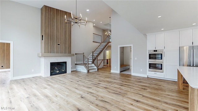 unfurnished living room featuring a glass covered fireplace, light wood-style flooring, stairway, a high ceiling, and a notable chandelier