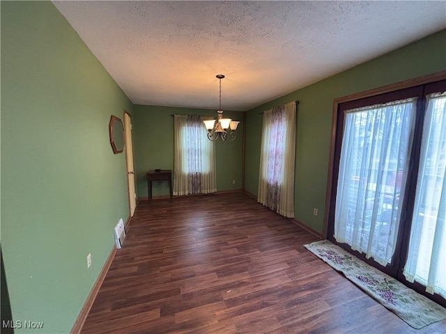 unfurnished dining area with a textured ceiling, wood finished floors, visible vents, a healthy amount of sunlight, and an inviting chandelier