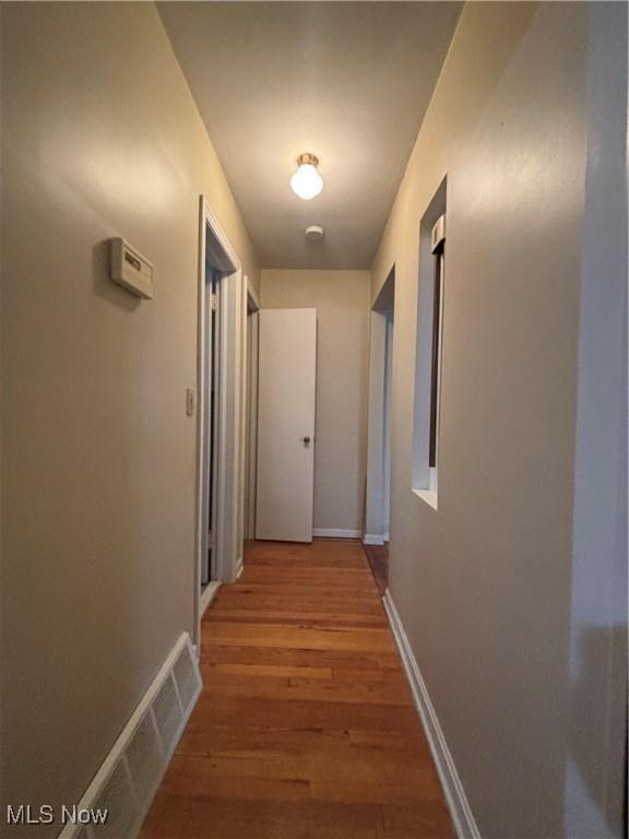 hallway featuring light wood-style floors, visible vents, and baseboards