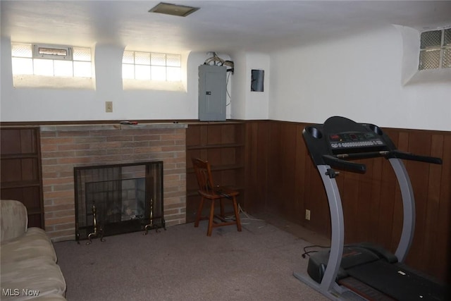 exercise room featuring wooden walls, a wainscoted wall, a fireplace, electric panel, and carpet