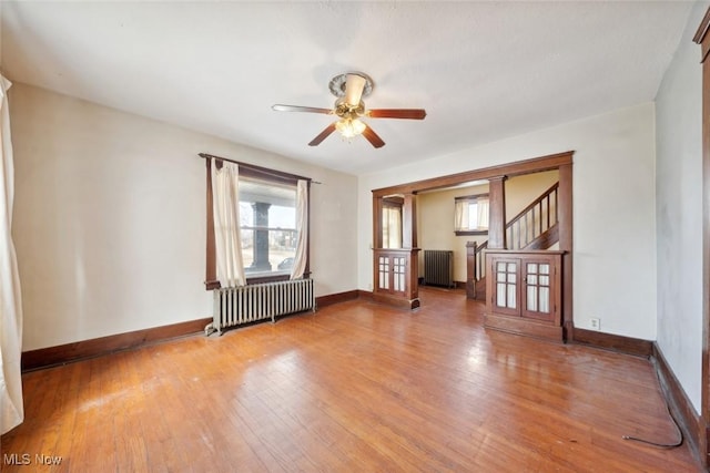 unfurnished room with ceiling fan, radiator heating unit, baseboards, and wood-type flooring