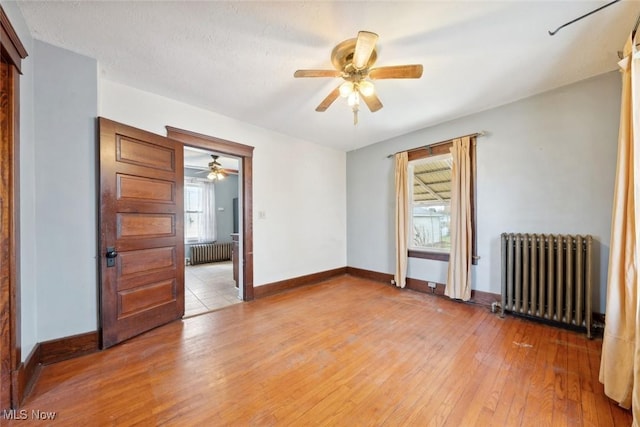 spare room with light wood-style floors, radiator, baseboards, and a ceiling fan