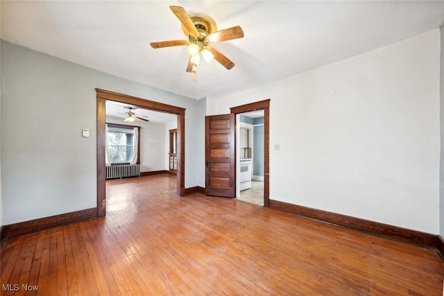 empty room with radiator, light wood finished floors, baseboards, and a ceiling fan