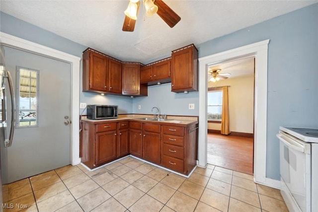 kitchen featuring light tile patterned floors, white range with electric cooktop, light countertops, stainless steel microwave, and a sink