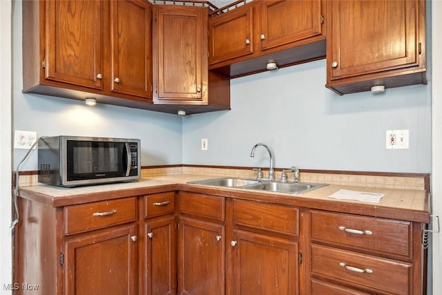 kitchen featuring brown cabinets, light countertops, stainless steel microwave, and a sink