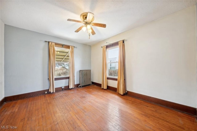 unfurnished room with baseboards, light wood-type flooring, a ceiling fan, and radiator