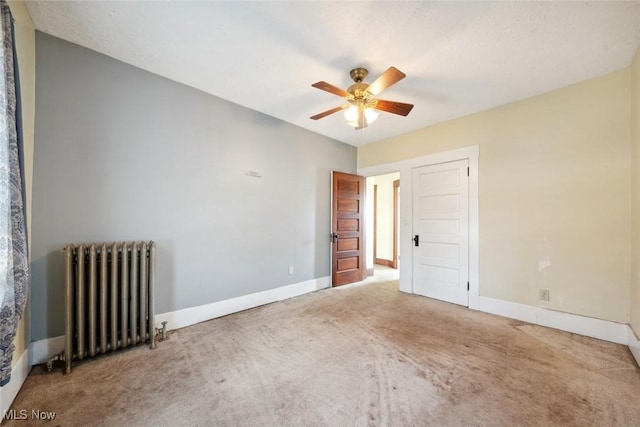 carpeted spare room with radiator, baseboards, and a ceiling fan