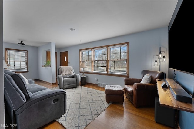 living room with a healthy amount of sunlight, baseboards, visible vents, and wood finished floors