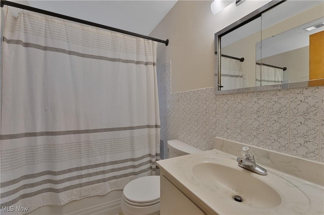 full bathroom with toilet, visible vents, tile walls, wainscoting, and shower / tub combo with curtain