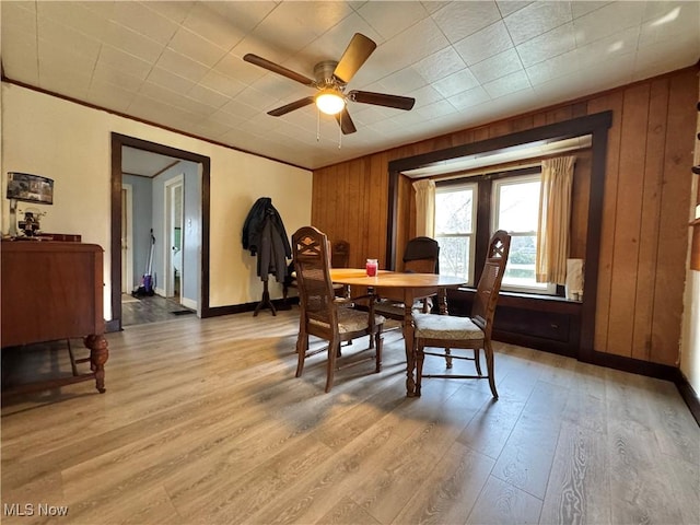 dining space with baseboards, ceiling fan, wood walls, and light wood-style floors