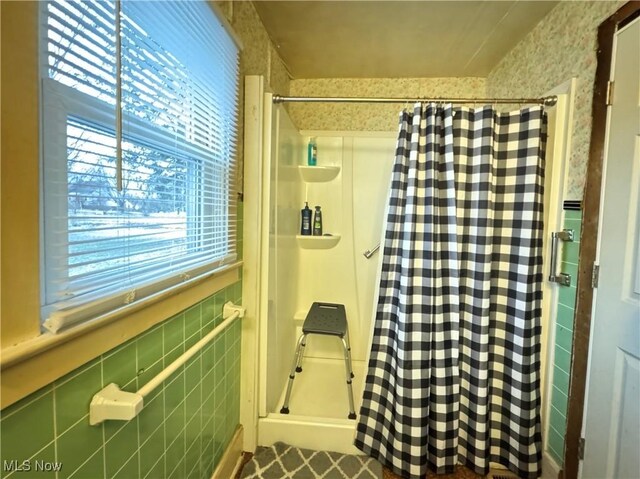 full bath with tile walls, a wainscoted wall, and a shower stall