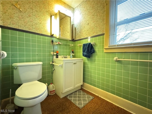 half bath with toilet, wallpapered walls, and wainscoting