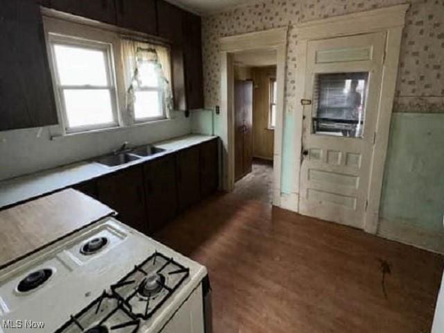 kitchen featuring light countertops, wallpapered walls, a sink, wood finished floors, and white gas range oven