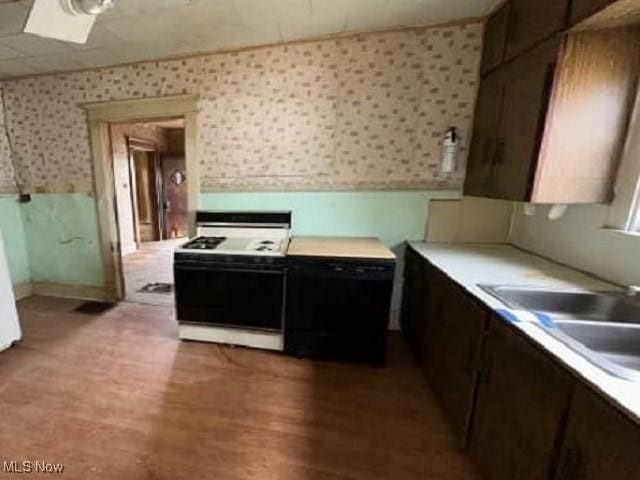 kitchen featuring light wood-style flooring, white range with gas stovetop, a sink, light countertops, and wallpapered walls