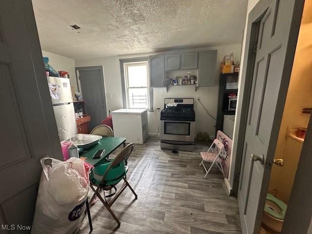 kitchen with a textured ceiling, gray cabinetry, refrigerator, stainless steel range with gas cooktop, and freestanding refrigerator