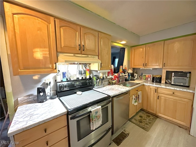 kitchen with light wood-style flooring, light brown cabinetry, appliances with stainless steel finishes, a sink, and under cabinet range hood