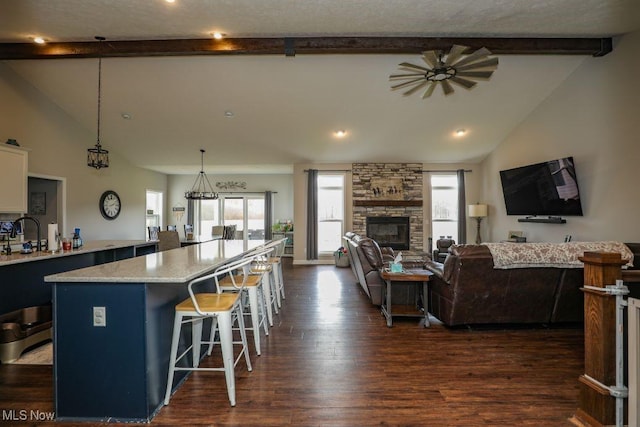 kitchen with a center island, dark wood finished floors, a breakfast bar, beam ceiling, and a fireplace