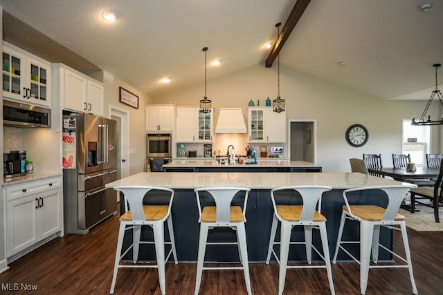 kitchen with vaulted ceiling with beams, a large island with sink, dark wood-type flooring, appliances with stainless steel finishes, and white cabinetry