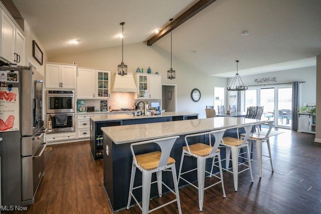 kitchen featuring tasteful backsplash, dark wood-type flooring, beamed ceiling, an island with sink, and appliances with stainless steel finishes