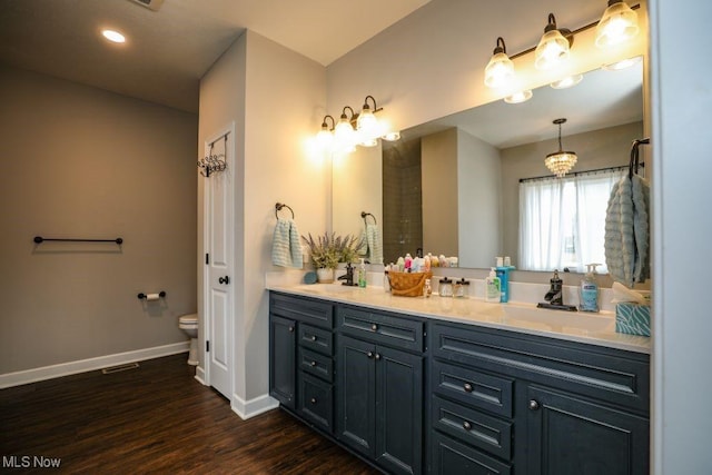 bathroom with toilet, a sink, wood finished floors, double vanity, and baseboards