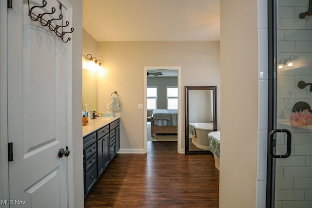 bathroom featuring a stall shower, wood finished floors, double vanity, baseboards, and a soaking tub