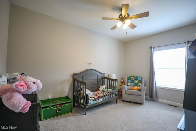 carpeted bedroom with visible vents, baseboards, a nursery area, and ceiling fan