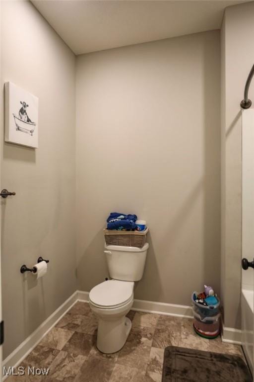 full bath with toilet, a tub to relax in, and baseboards