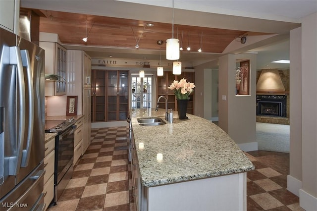 kitchen featuring stainless steel fridge, electric range, a kitchen island with sink, a fireplace, and a sink