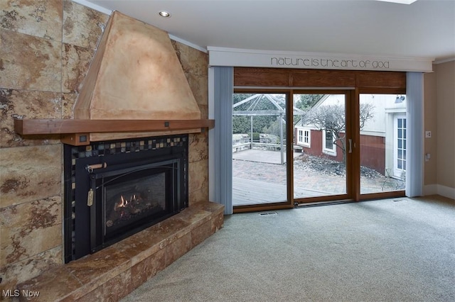 unfurnished living room with carpet floors, crown molding, a fireplace, visible vents, and baseboards