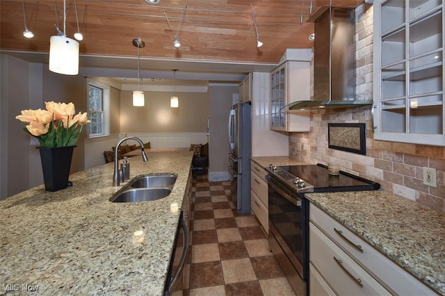 kitchen with dark floors, stainless steel appliances, glass insert cabinets, a sink, and wall chimney exhaust hood