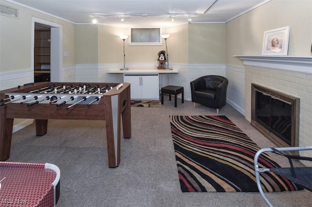 game room with ornamental molding, a wainscoted wall, a fireplace, and track lighting