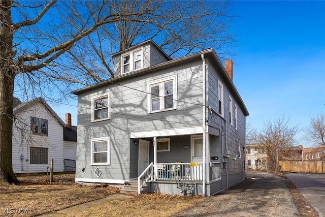 american foursquare style home with covered porch, driveway, and a chimney