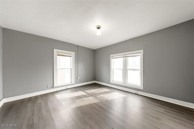 empty room featuring a textured ceiling, baseboards, and dark wood-style flooring