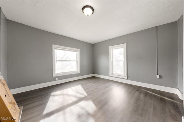 unfurnished room with a textured ceiling, wood finished floors, and baseboards