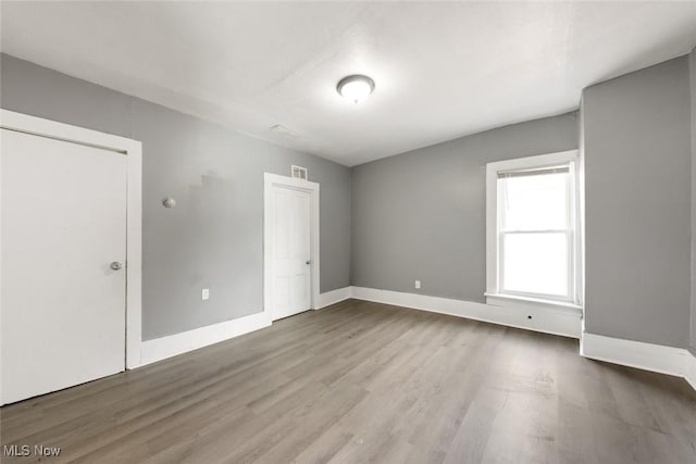 spare room with wood finished floors, visible vents, and baseboards