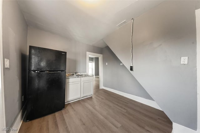 kitchen featuring light countertops, freestanding refrigerator, white cabinetry, light wood-type flooring, and baseboards