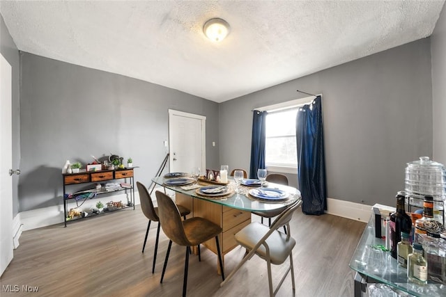 dining space with a textured ceiling, baseboards, and wood finished floors