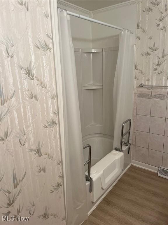 bathroom with shower / tub combo, wood finished floors, visible vents, tile walls, and ornamental molding