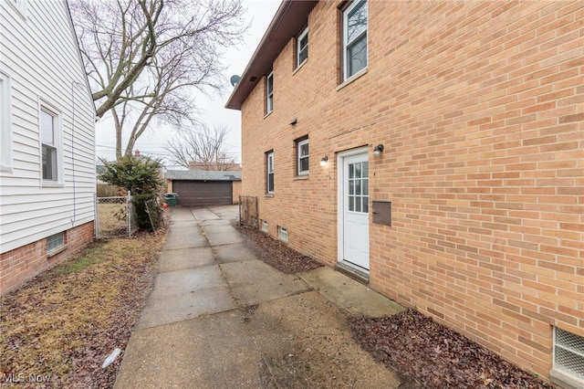 view of side of property with a detached garage, fence, an outbuilding, and brick siding