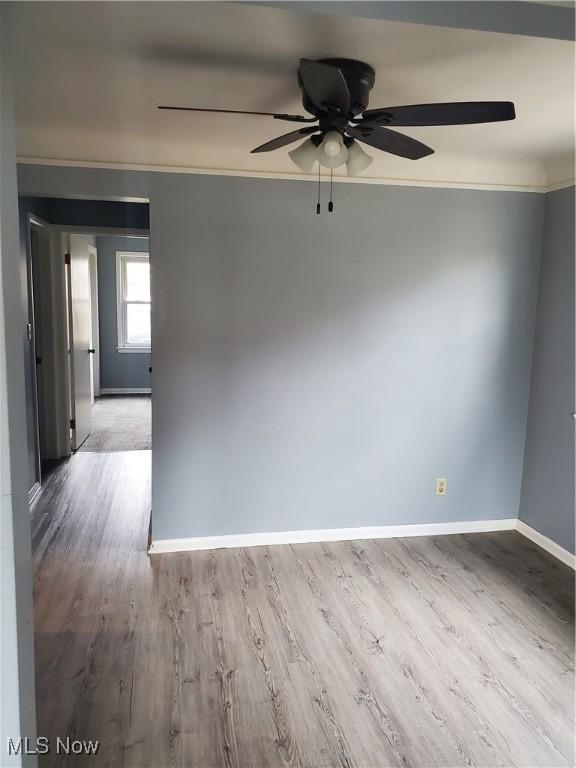 empty room with baseboards, ceiling fan, wood finished floors, and crown molding