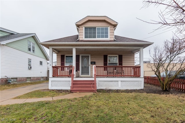 bungalow-style house with covered porch, roof with shingles, fence, and a front lawn