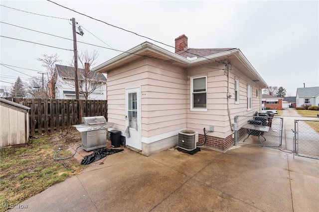 rear view of property with a chimney, a gate, fence, a patio area, and central AC