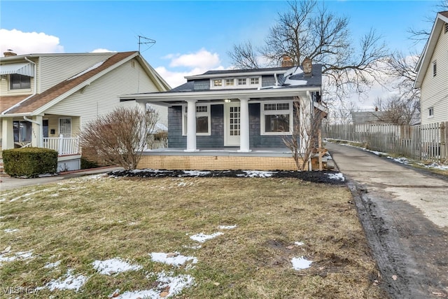 view of front facade with covered porch, a chimney, a front yard, and fence